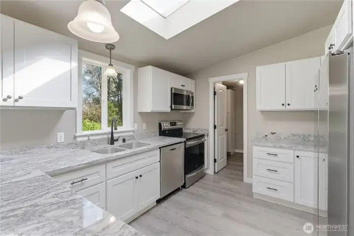 These beautiful neutral grey and white counter tops, deep double sink with black fawcet. Stainless dishwasher, and refrigerator compliment the color concept and the black/and stainless stove and microwave.  Door leads into the back door entry with cabinet storage.