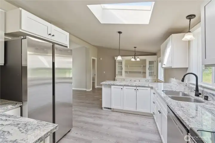 Looking from the kitchen into the adjoining dining and open living area.  The stainless refrigerator has two large side by side doors and great lighting and space inside.