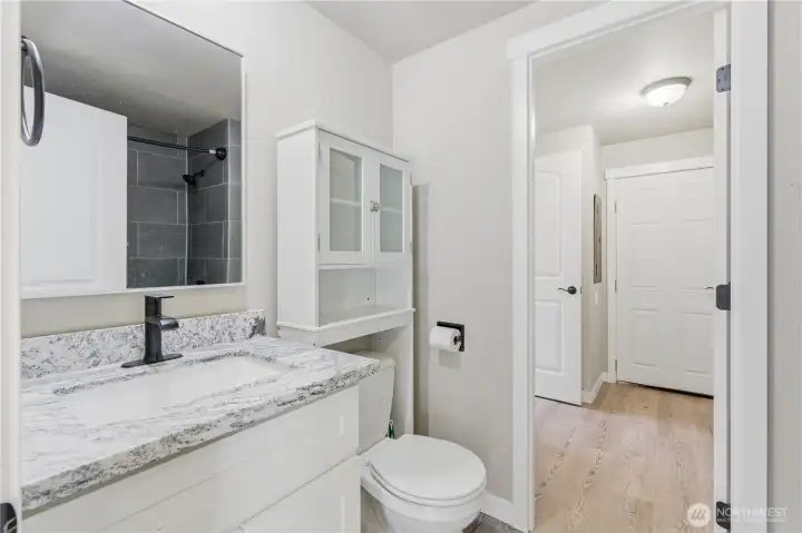 2nd bathroom has access from washing room, outside and kitchen and on the other side access is from the hallway to the two extra bedrooms.  Shower/tub area has grey/black tiles which compliments the countertops.