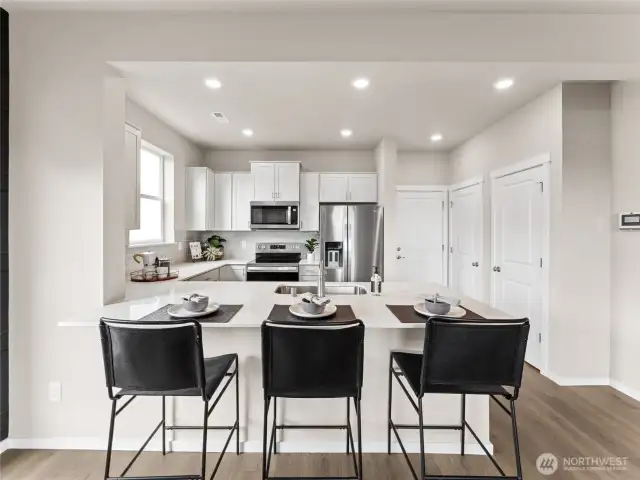 Quartz-topped island seats four and anchors a stainless-appliance kitchen framed by bright shaker cabinetry. Pictures are for representational purposes only, colors and features may vary.