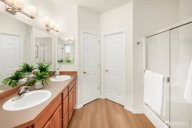 Primary dual sink vanity, walk in shower, luxury plank flooring, a linen closet to the left and the walk-in closet behind the closed door on the right.