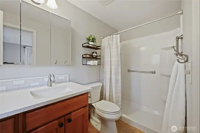 Updated primary bath en suite offers a spacious shower and tall vanity with quartz.  Mirror provides additional storage behind, and window offers natural light.