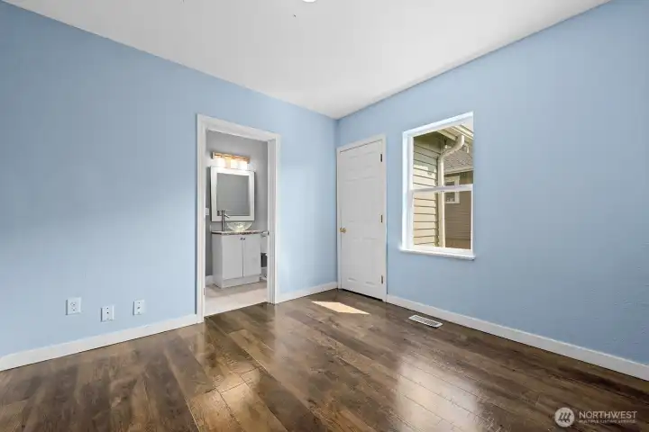 Freshly painted in soft blue tones, this cozy bedroom features warm wood flooring, a closet, and direct access to a private bath.