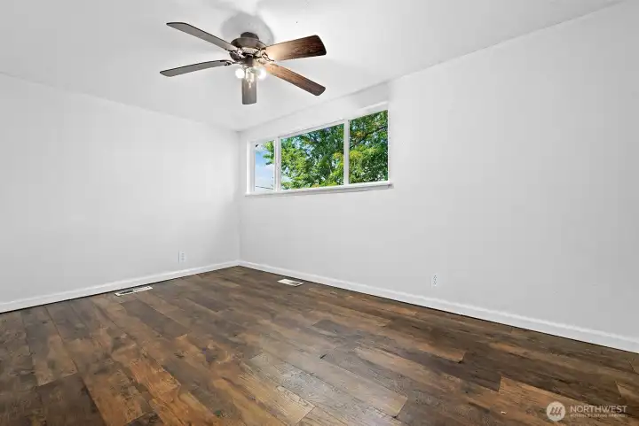bedroom retreat with warm wood floors, ceiling fan, and large window bringing in natural light.