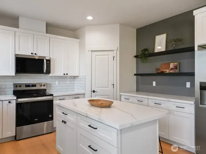 Island in Chef's kitchen with seating. Stainless Appliances include the Fridge.  Additional Counter & Cabinet Space with floating shelves is an added plus.
