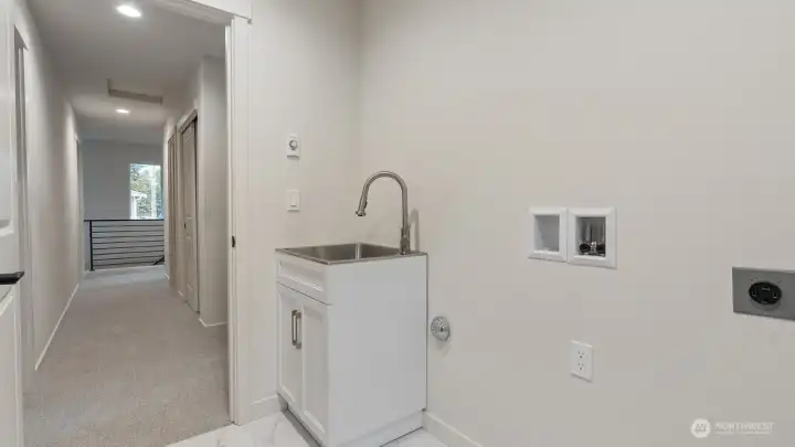 2nd floor laundry room has utility sink with cabinet and tile flooring.