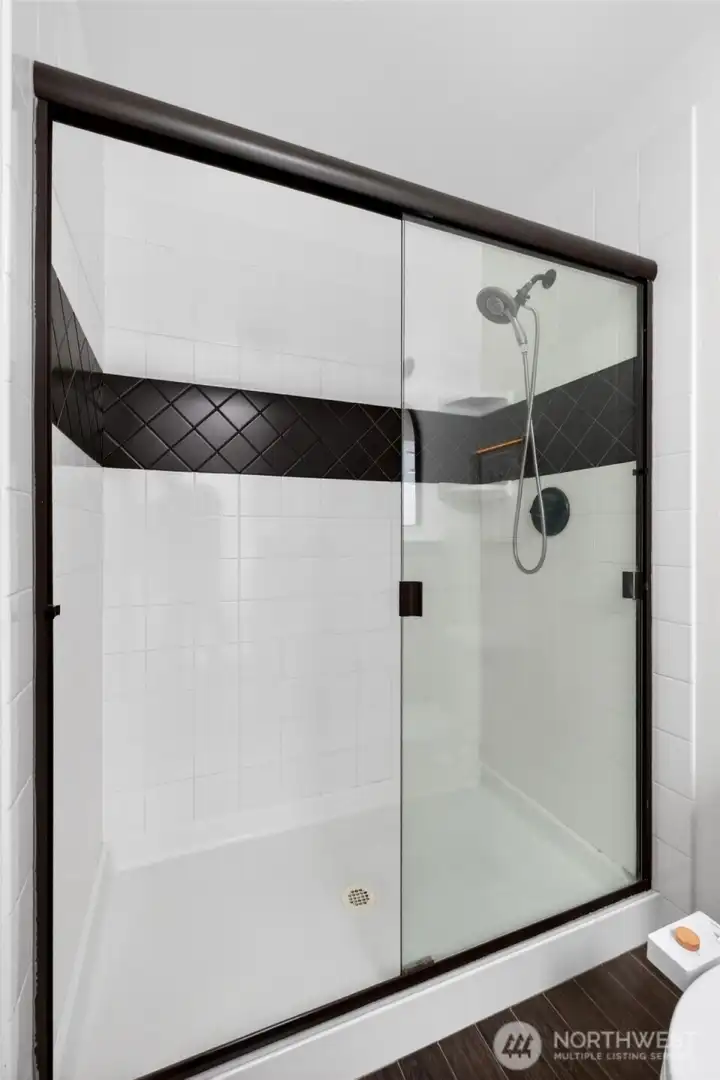 A spacious glass-enclosed shower with crisp tile work and a bold accent band creates a clean, modern look. The design feels fresh and timeless, offering both style and easy maintenance.