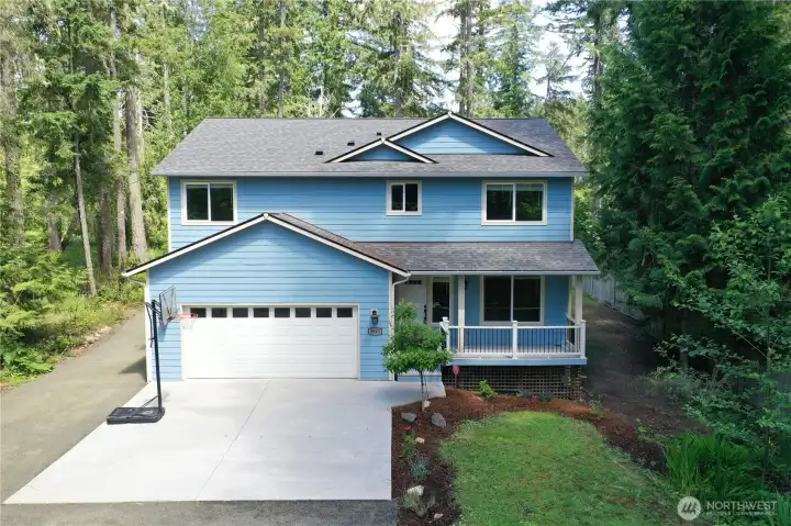 Front elevation with attached two-car garage and wooded surroundings.