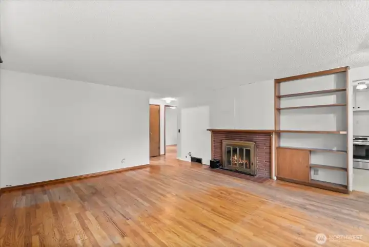 Spacious living room featuring hardwood floors, a brick fireplace, and built-in shelving with storage.