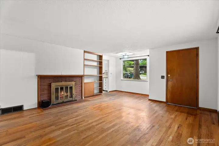 Another view of the main living area showcasing the fireplace, built-in cabinetry, and natural light from the front window.