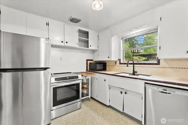 Kitchen featuring stainless steel appliances, extensive cabinet space, and a window overlooking the front yard.