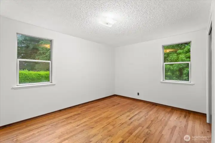 Bedroom with hardwood floors, fresh paint, and windows overlooking mature landscaping.