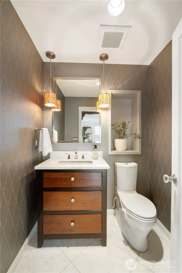 The powder room with stone flooring features a lovely vanity, art niche and decorative wallpaper & accents