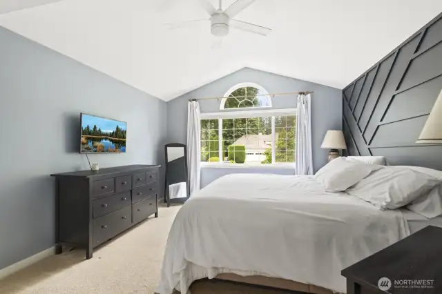 Upstairs, the luxurious primary suite is a  private retreat with soaring vaulted ceiling and custom wood-accent wall.