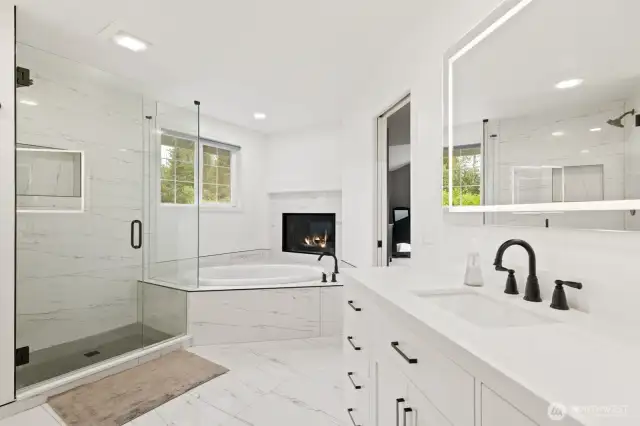 Newly remodeled, the ensuite features a designer-tiled shower with seamless glass enclosure and soaking tub in front of the fireplace.