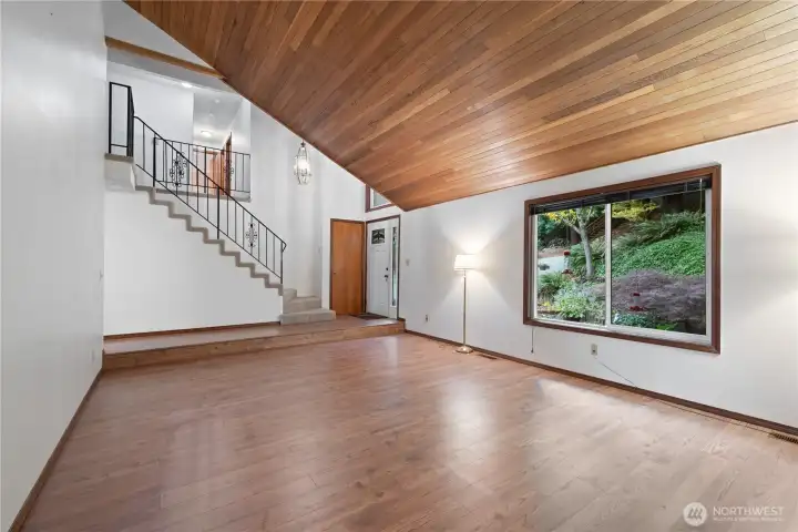 Living room with laminate flooring, cedar vaulted ceiling, built in bookcases and a wood burning fireplace