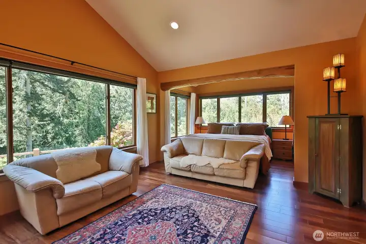 Primary Bedroom looking out upon the Northwest view of the property. A freestanding propane stove is just beyond the left edge of this photo. Across the hall from the Primary Suite is the Laundry Room and a door to the wrap around deck and easy access to the outdoor shower. Primary Bedroom looking out upon the Northwest view of the property. A freestanding propane stove is just beyond the left edge of this photo. Across the hall from the Primary Suite is the Laundry Room and a door to the wrap around deck and easy access to the outdoor shower.