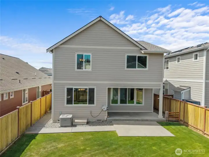 The rear exterior of the home features durable lap siding, large windows that flood the interior with natural light, a covered patio, and a full concrete pad — all set within a fully fenced yard. Clean, low-maintenance construction built for Pacific Northwest living.