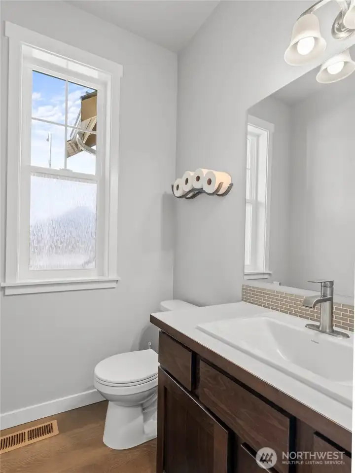The half bathroom on the main floor offers a clean, modern feel with a rich dark-stained vanity & tile backsplash. The window has a film for added privacy while still providing ample light.