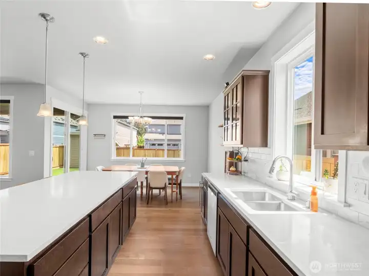 Another angle of the kitchen highlights the expansive island, glass-front upper cabinets, open shelving, and a wine refrigerator (Doesn't convey)— ideal for those who love to cook and entertain. The seamless flow into the dining area makes hosting effortless.