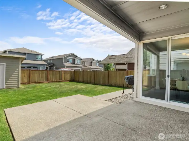 Enjoy the fully fenced backyard featuring a lush green lawn, covered concrete patio with recessed lighting, and a sliding glass door leading directly into the dining area. A great space for entertaining, kids, or pets — all with the privacy of a wood fence.