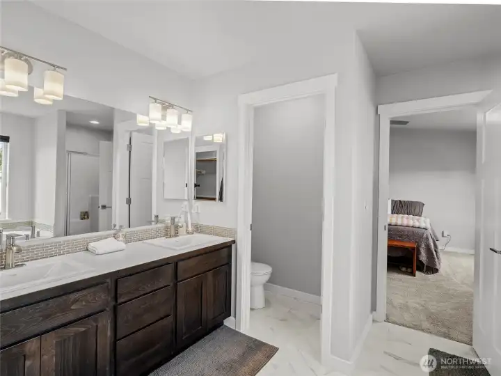 Full view of the primary en suite showcasing the double vanity, private water closet, and seamless connection to the primary bedroom. Thoughtfully designed with dual storage and an open, bright layout.