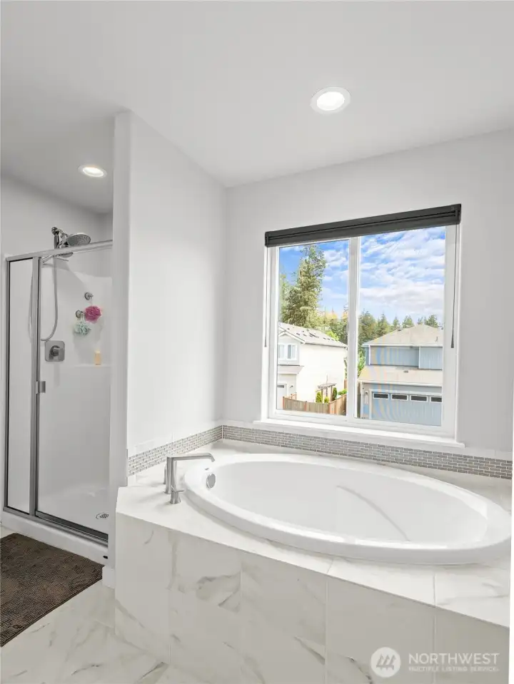 Relax in style with this soaking tub set against marble-look tile and surrounded by natural light from a large window. A separate glass-enclosed shower adds convenience, making this primary bath a true sanctuary.