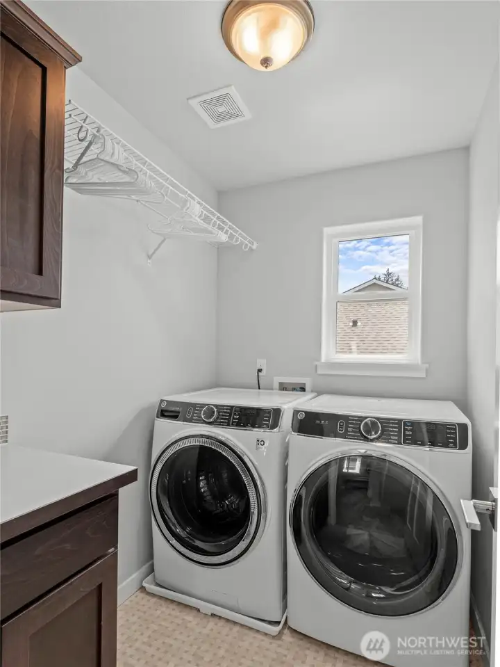The upstairs laundry room is a standout feature, complete with GE front-load washer and dryer (Conveys with home), dark cabinetry with countertop workspace, hanging rod, and a window for natural light. Laundry day has never been this convenient.