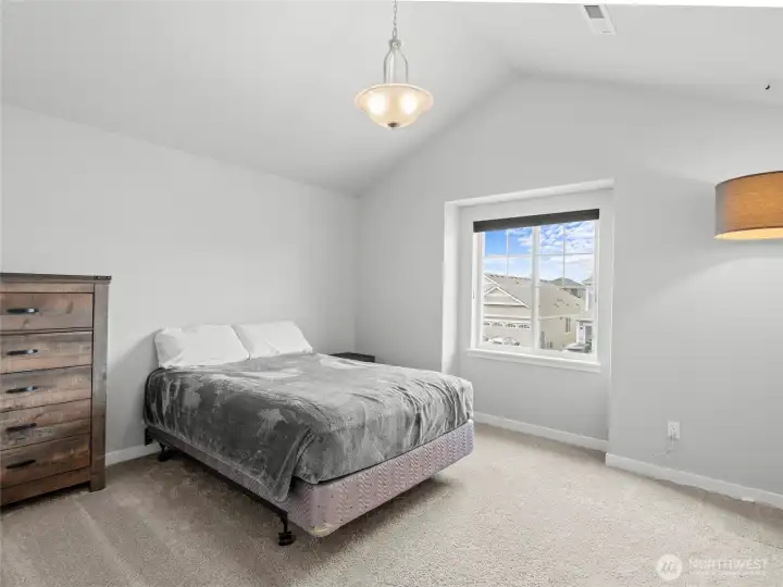 Spacious fourth bedroom features vaulted ceilings, plush carpet, a stylish pendant light fixture, and a bright window with neighborhood views. A comfortable and versatile room that works well as a guest suite, teen bedroom, or additional flex space.