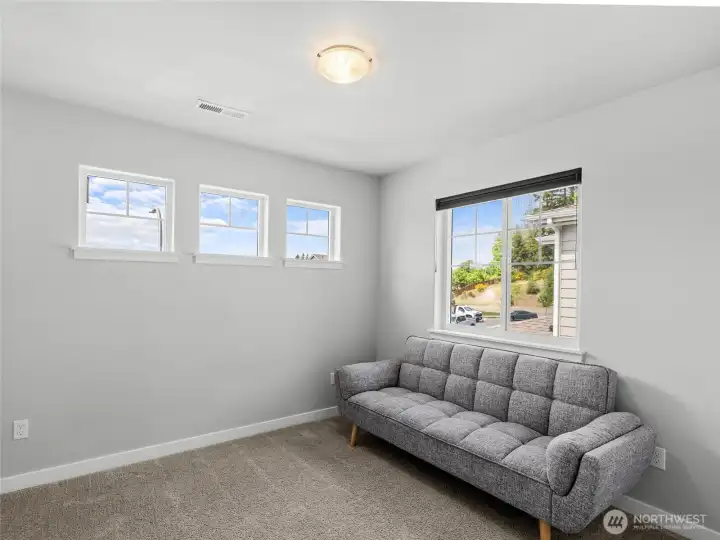 Second view of the fifth bedroom showcases the generous natural light from multiple windows, including a charming trio of smaller windows offering a peek of the neighborhood and greenery beyond. A bright, welcoming space with great flexibility.