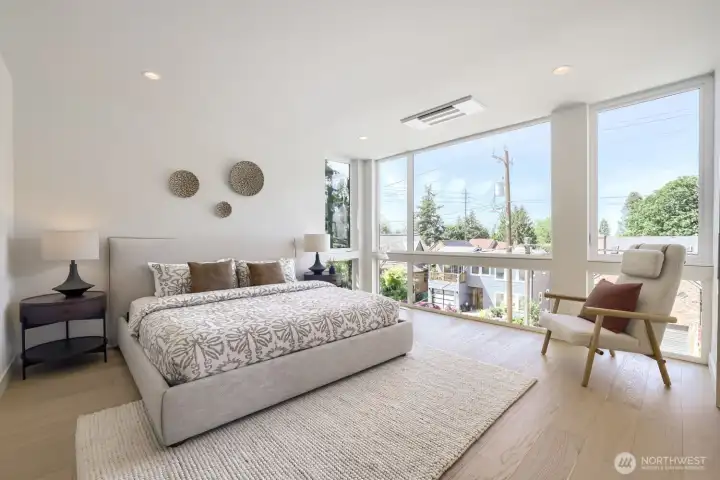 A luxurious primary bedroom with floor-to-ceiling windows bring in the outdoors.