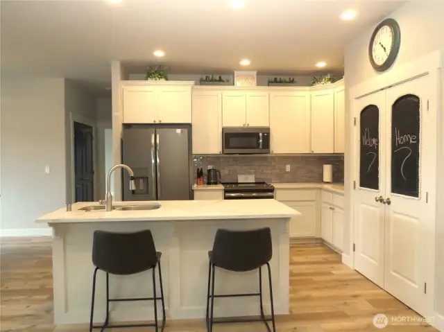 THE GREAT ROOM INCLUDES THIS GORGEOUS BRIGHT KITCHEN WITH SLAB COUNTER TOPS, WHITE CABINETRY, BLACK APPLIANCES, PLUS DOUBLE DOOR PANTRY!