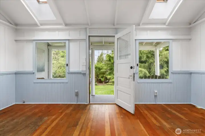 A view from the living room and eating space to the front door and front porch.  Note the 2 skylights above, and the vaulted ceilings.  This room also has a cozy wood stove, suitable for heating the entire home.  This room is 17' x 12', the porch is 16'11" x 5'6".  Look at those fir floors - refinishing will make them gleam!