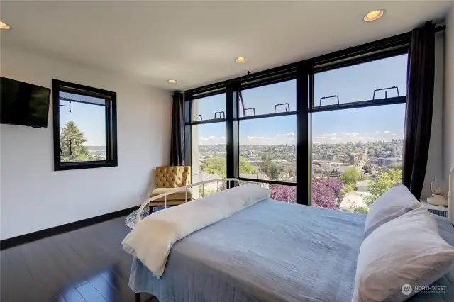 The primary suite enjoys a wall of windows showcasing city and mountain views.