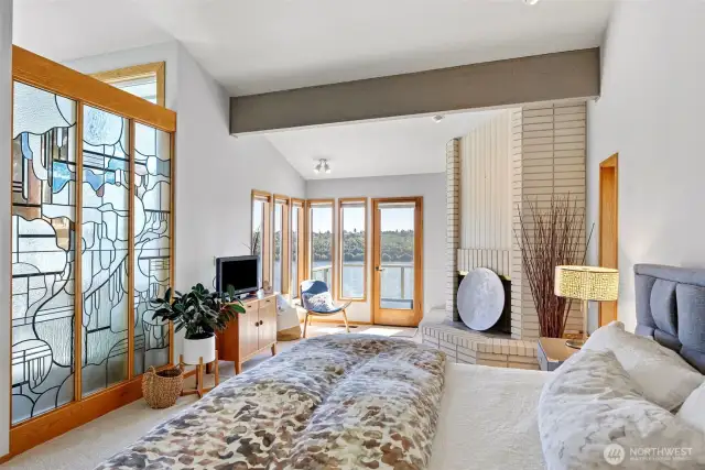 Soaring ceilings, wood beams, wood-burning fireplace, and a stained-glass wall make this primary suite special.