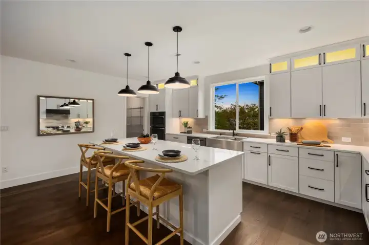 Kitchen Island & Window View: Sleek farmhouse sink beneath a wide window complements quartz counters and designer cabinetry. Casual bar seating at the island adds functionality and creates a perfect gathering spot while cooking or entertaining.    Photos are from the model home at Foxmoore and for visualization purposes only. Plans, colors, building orientation, finishes, home outlook, and other details can and WILL vary.