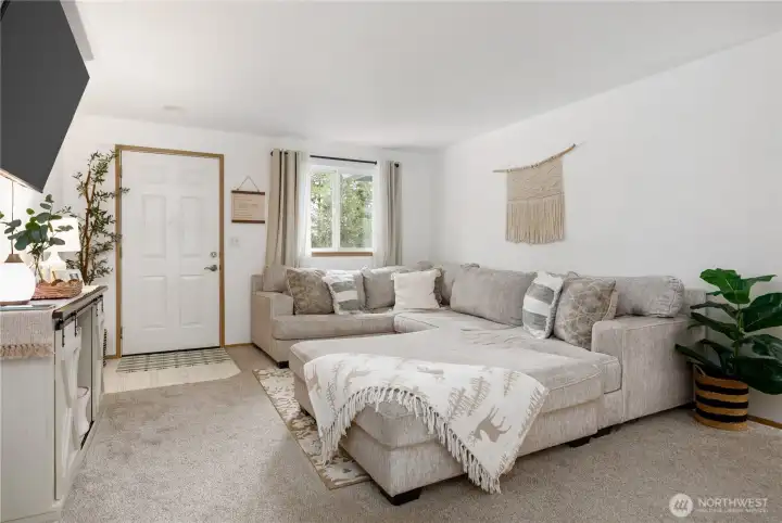 A spacious, bright, and airy living room that feels both cozy and open — perfect for relaxing or entertaining. Sunlight pours in, highlighting comfortable seating and soft textures, while sightlines flow gracefully to the dining room and kitchen, keeping conversation and company connected. It’s an inviting, effortless space where cozy evenings and lively gatherings feel equally at home.