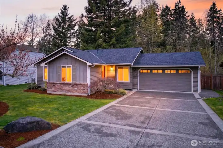 Warm evening light spills through the windows of this charming English Hill rambler, framed by mature evergreens and a lush, level front lawn that sets the stage for easy Eastside living. The wide concrete driveway and oversized two-car garage offer the storage and convenience that buyers in Redmond genuinely appreciate.