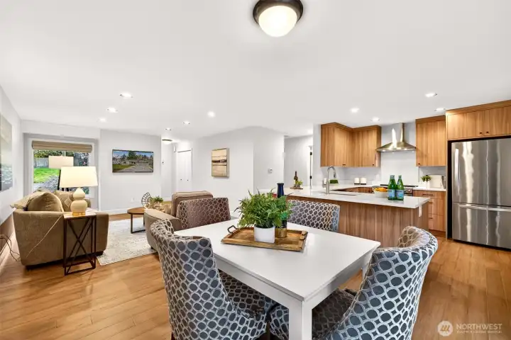 This angle captures the full depth of the open-concept main level — from the updated kitchen with stainless refrigerator and custom walnut cabinetry all the way through to the living area — demonstrating just how livable and connected the floor plan truly is. Updated hardwood flooring ties the entire space together with warmth and continuity.
