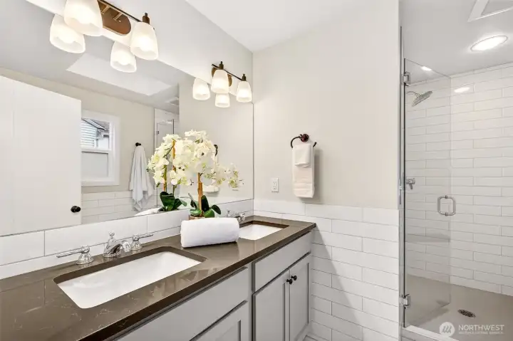 Fully reconfigured and updated in 2019, the primary 3/4 bath features a double vanity with rich dark quartz countertops, subway tile surround, and a glass-enclosed walk-in shower — a spa-caliber finish rarely seen at this price range. The clean white palette and quality fixtures make this one of the standout spaces in the home.