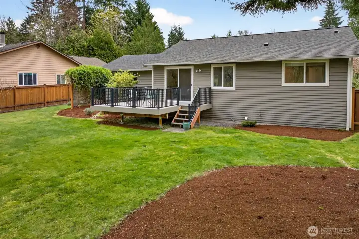 The full width of the rear yard is on display here — a well-proportioned, fully fenced space with fresh mulch beds framing the lawn and a composite deck positioned perfectly for relaxing or entertaining. The 2021 roof overhead and updated siding details confirm that the exterior has been thoughtfully maintained throughout.