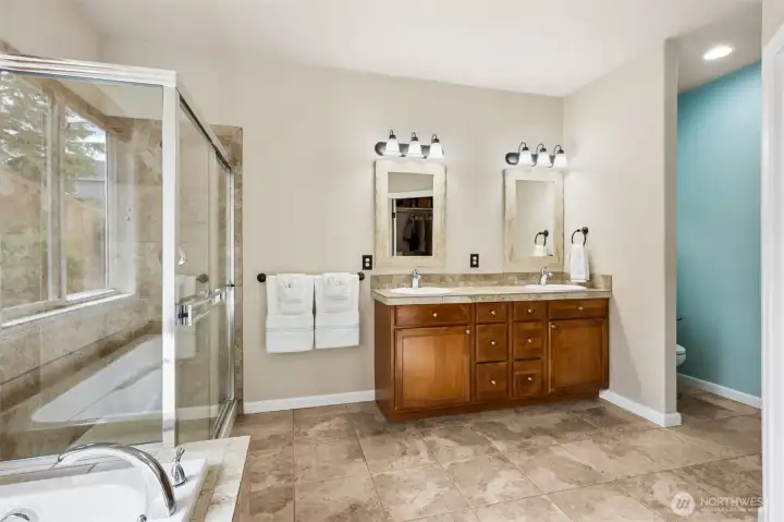 Very large primary suite with dual vanity area, custom mirrors, ceramic tile floors & tucked away toilet area.