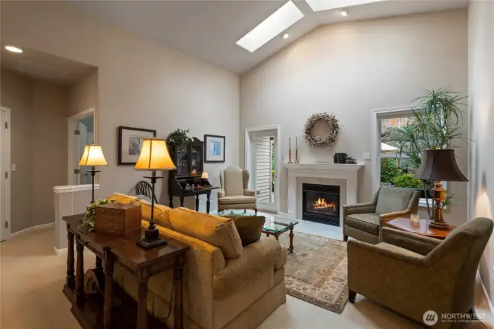 Living area in the great room with vaulted ceilings and skylights for natural light.  Detailed millwork surrounds the gas fireplace with access to lovely side patio & garden thru door on the left.