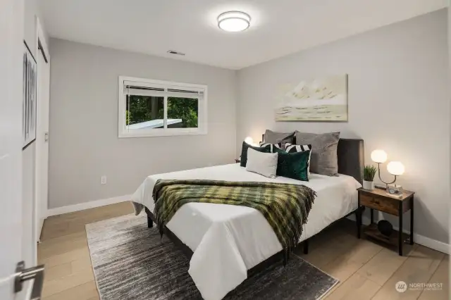 The first upstairs bedroom welcomes you with the same luxurious laminate flooring that graces the rest of the house. A large window offers a serene view of the surrounding trees, creating a peaceful and inviting atmosphere.