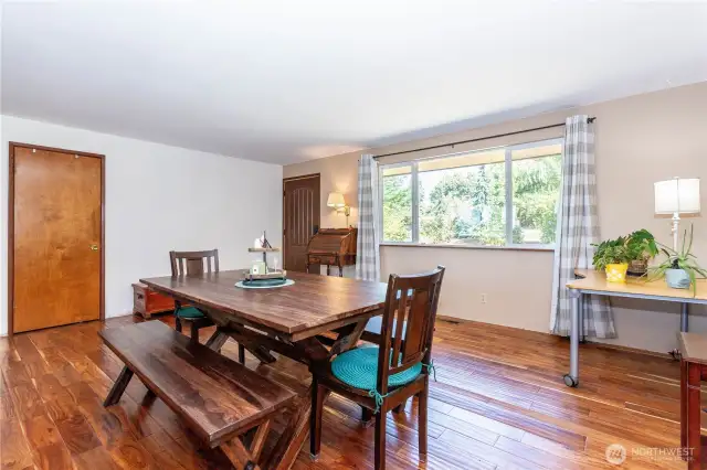 This dining area is bright and inviting, anchored by a large window that frames greenery outside and fills the room with natural light. The open layout creates an easy flow for entertaining, while warm-toned wood floors add character. Neutral walls make it a versatile space that can adapt to any design style. Whether you host family dinners or casual get-togethers, this room offers the perfect backdrop for gatherings with plenty of natural charm.