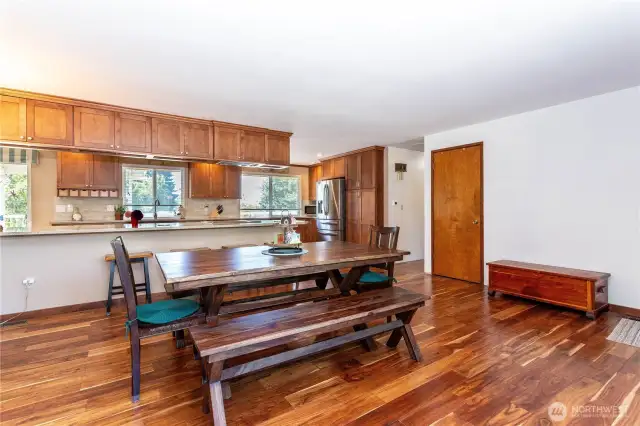 Here, you see how the dining space flows seamlessly into the kitchen. The warm wood cabinetry pairs beautifully with stone countertops, creating a timeless design. The large island doubles as a breakfast bar, making this the heart of the home for meals and conversation. The open-concept design allows for connection, so whether cooking or dining, everyone is part of the same space. The layout is functional, welcoming, and perfect for both everyday living and hosting.