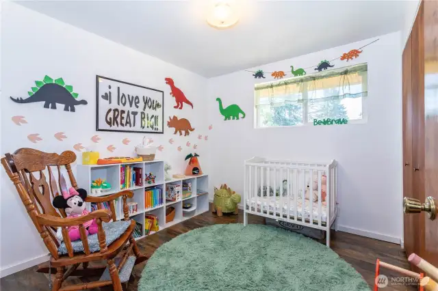 The nursery offers a cheerful and cozy space with natural light pouring in. Decorated with a playful dinosaur theme, it highlights how versatile the bedrooms are for any stage of life. The warm wood floors create a natural contrast with bright white walls, making the space feel light and airy. This room demonstrates not only the size of the bedrooms but also their adaptability, whether used as a child’s room, guest space, or creative retreat.
