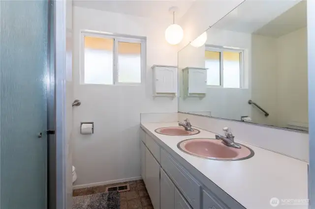 This bathroom showcases double sinks with vintage charm and functionality. Large mirrors and built-in cabinetry provide both space and convenience. The layout is simple yet efficient, with a shower and window for light and ventilation. The retro details, like the pink basins, give a nostalgic feel while offering an opportunity for creative updates. It’s a practical bathroom that’s move-in ready but also primed for modernization.