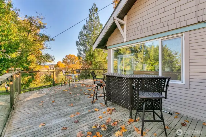 Expansive wraparound deck with clear panel railing along the north & east sides, leading to the front entrance.