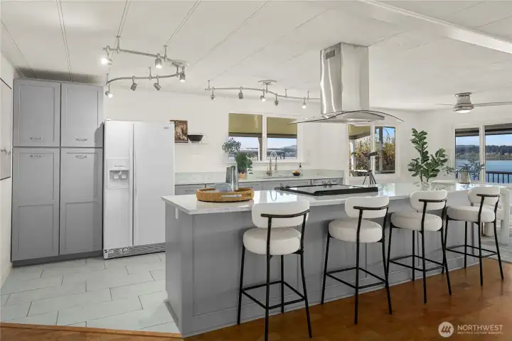 The beautifully remodeled kitchen features an oversized island with seating, a sleek glasstop range, and a modern SS/glass vent—perfect for casual dining and entertaining.